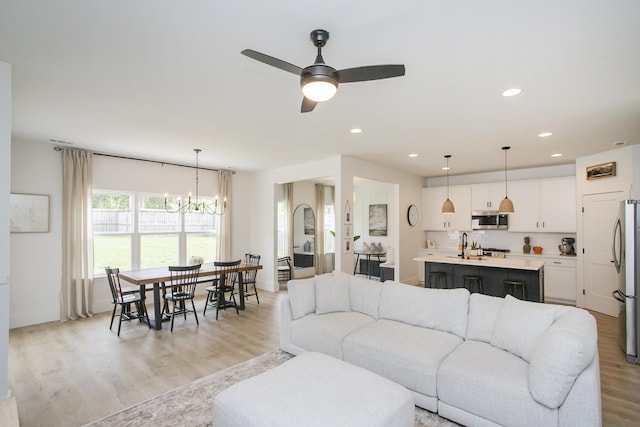 living area featuring recessed lighting, baseboards, ceiling fan with notable chandelier, and light wood-style flooring