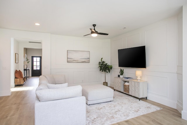 living room featuring light wood finished floors, recessed lighting, ceiling fan, and a decorative wall