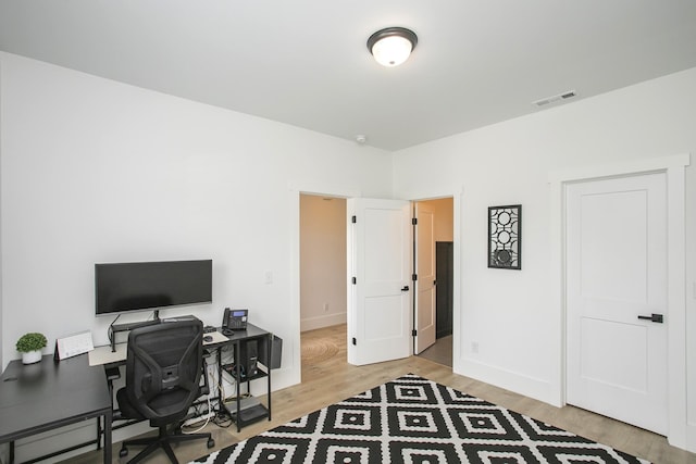 office space featuring baseboards, light wood-style flooring, and visible vents