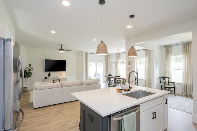 kitchen featuring a sink, open floor plan, light wood-style flooring, light countertops, and appliances with stainless steel finishes