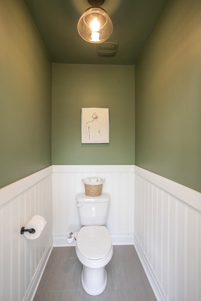 bathroom with a wainscoted wall, toilet, visible vents, tile patterned flooring, and a decorative wall