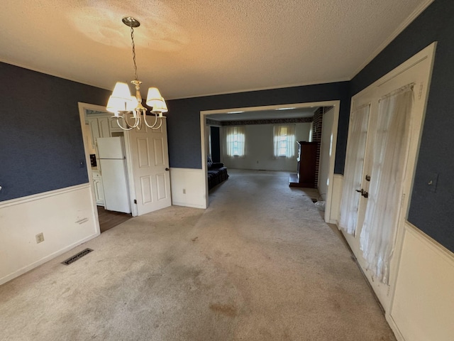 unfurnished dining area featuring a chandelier, a textured ceiling, visible vents, wainscoting, and carpet