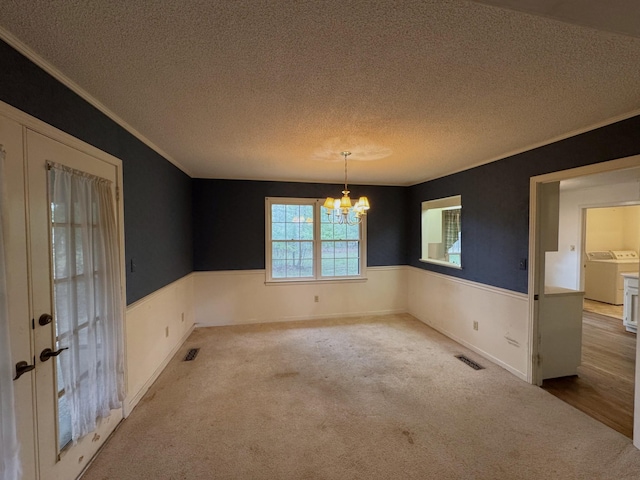 empty room with a chandelier, carpet floors, washer / dryer, wainscoting, and visible vents