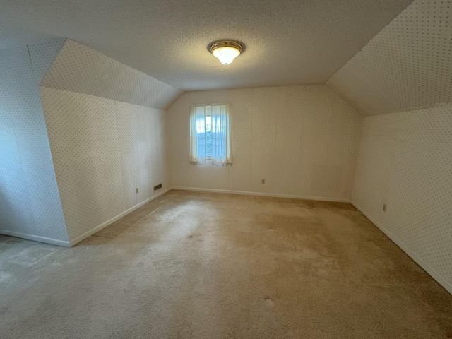 additional living space with wallpapered walls, baseboards, light colored carpet, and lofted ceiling