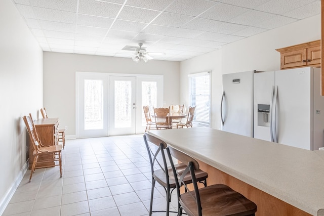 dining room with light tile patterned floors, a drop ceiling, baseboards, and ceiling fan