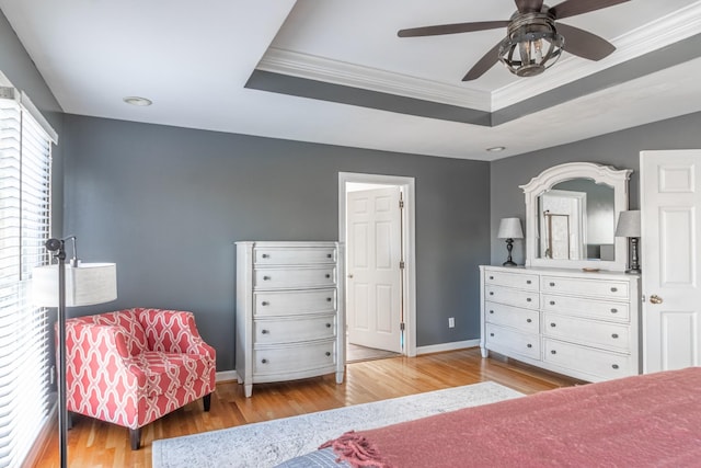 bedroom featuring baseboards, light wood-style flooring, a tray ceiling, and crown molding