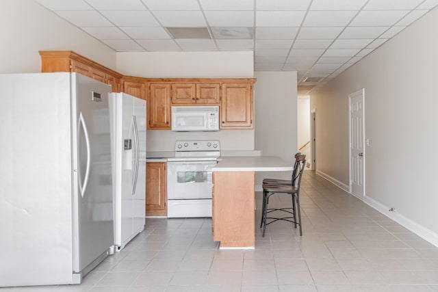 kitchen featuring white appliances, light countertops, a breakfast bar area, and light tile patterned flooring