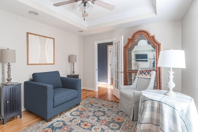 living room featuring crown molding, ceiling fan, light wood-type flooring, a raised ceiling, and baseboards