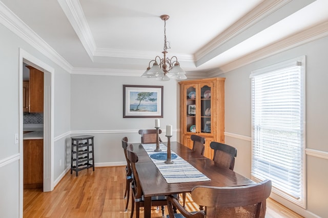 dining area with a raised ceiling, a notable chandelier, crown molding, and light wood-style flooring
