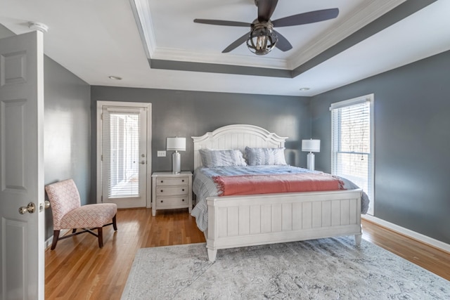 bedroom with a tray ceiling, crown molding, wood finished floors, and baseboards