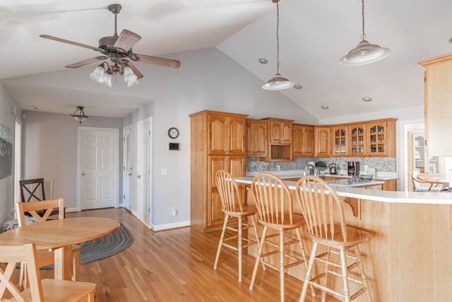kitchen featuring glass insert cabinets, a kitchen breakfast bar, tasteful backsplash, light wood-type flooring, and light countertops