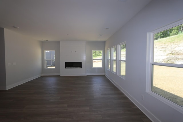 unfurnished living room featuring dark wood-type flooring, baseboards, and plenty of natural light
