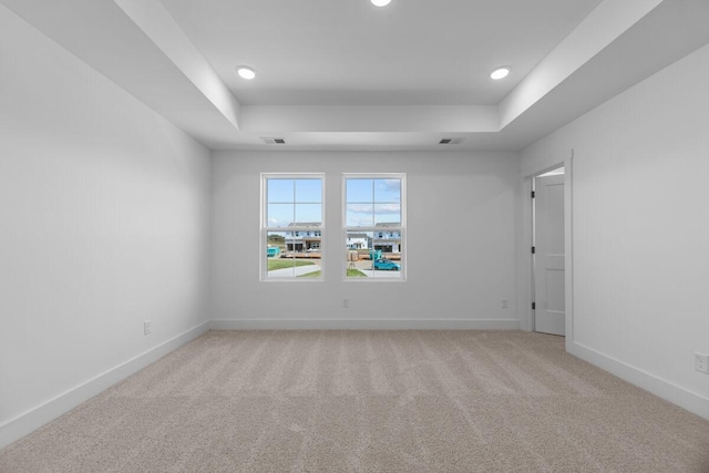 empty room with light colored carpet, baseboards, and a raised ceiling