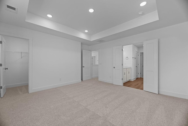 unfurnished bedroom with carpet, a raised ceiling, visible vents, a walk in closet, and baseboards