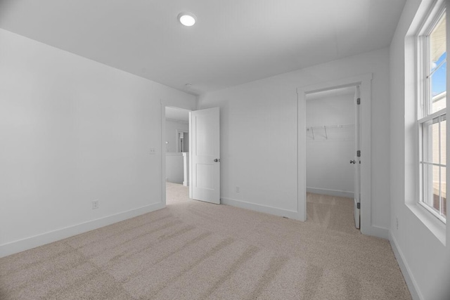 unfurnished bedroom featuring a closet, baseboards, a spacious closet, and light colored carpet