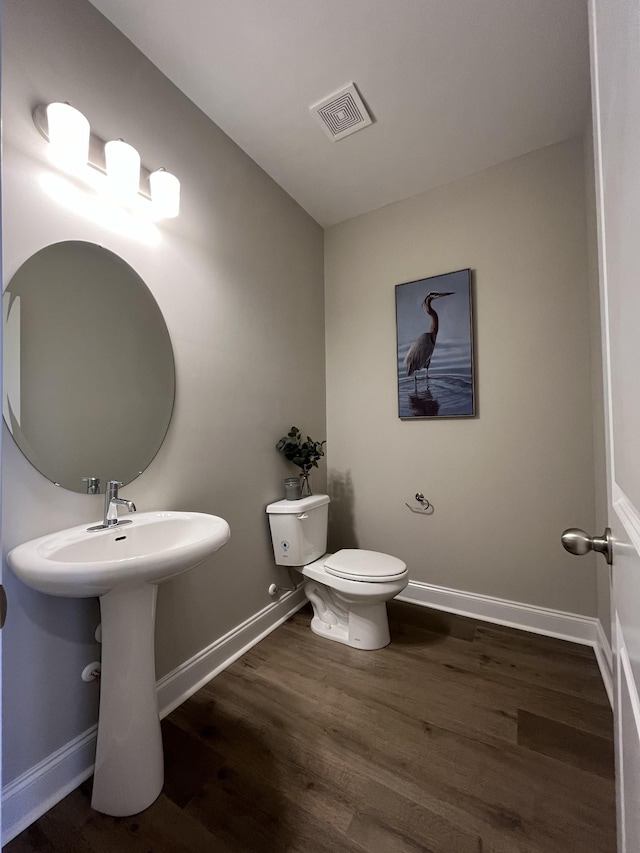 bathroom with baseboards, toilet, visible vents, a sink, and wood finished floors