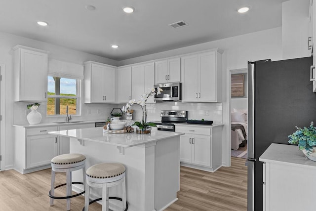 kitchen with light wood-type flooring, white cabinetry, visible vents, appliances with stainless steel finishes, and a sink