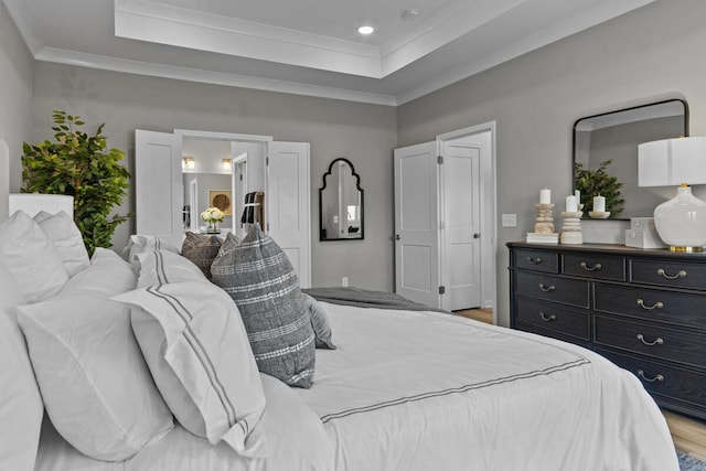 bedroom with a tray ceiling, wood finished floors, ornamental molding, and recessed lighting