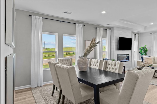 dining area featuring visible vents, a raised ceiling, light wood-type flooring, recessed lighting, and a glass covered fireplace