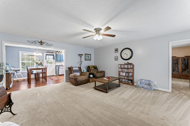 living room with baseboards, a textured ceiling, carpet, and ceiling fan