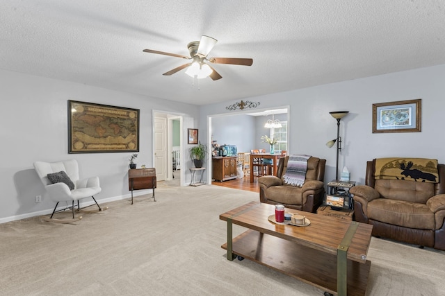 living room featuring baseboards, ceiling fan with notable chandelier, a textured ceiling, and light colored carpet