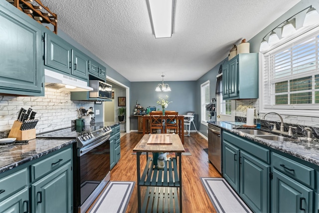 kitchen featuring a textured ceiling, tasteful backsplash, a sink, under cabinet range hood, and stainless steel appliances