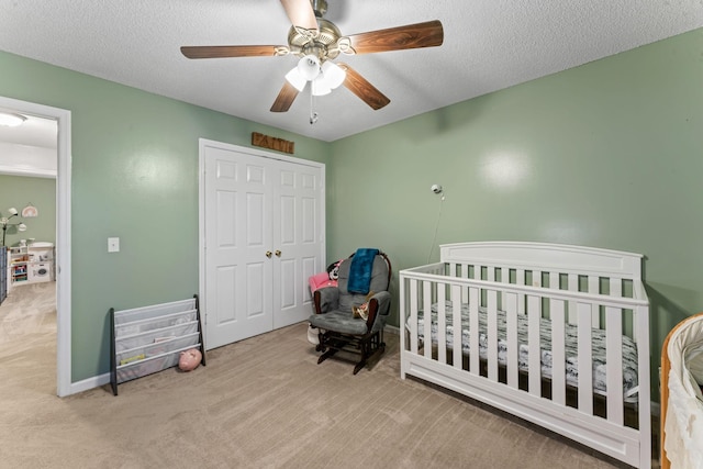 carpeted bedroom with a nursery area, a ceiling fan, a closet, and a textured ceiling