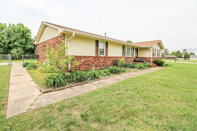 view of side of property featuring fence, a yard, and brick siding