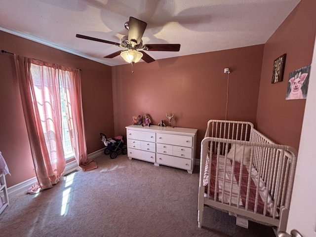carpeted bedroom with a nursery area, baseboards, multiple windows, and a ceiling fan