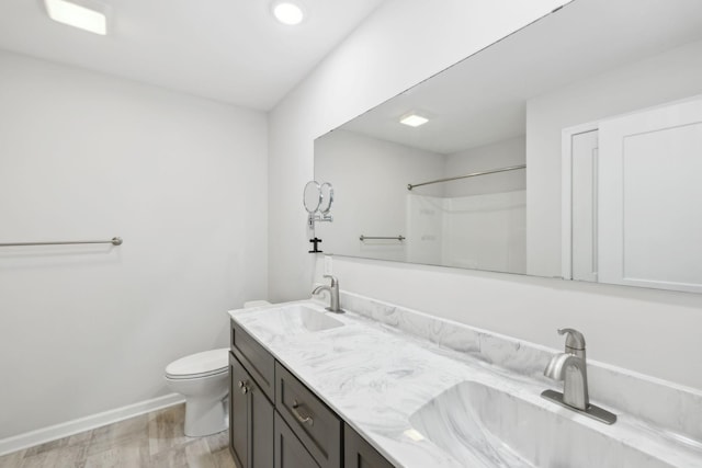 bathroom featuring toilet, double vanity, a sink, and baseboards