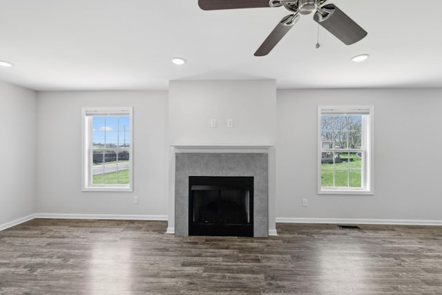 unfurnished living room with ceiling fan, a healthy amount of sunlight, wood finished floors, and a fireplace