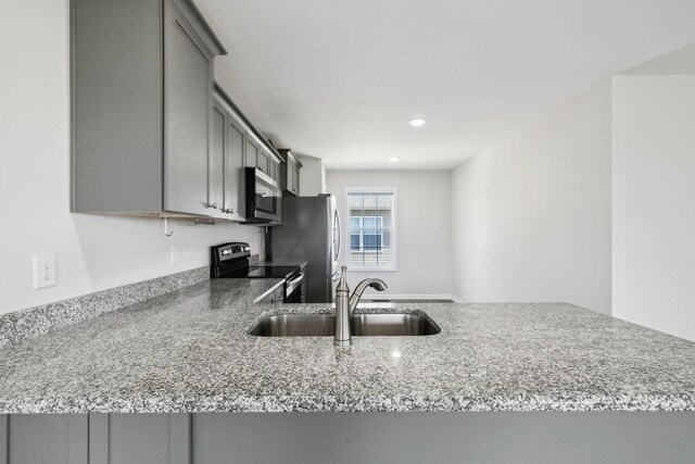 kitchen featuring light stone counters, recessed lighting, gray cabinetry, stainless steel appliances, and a sink
