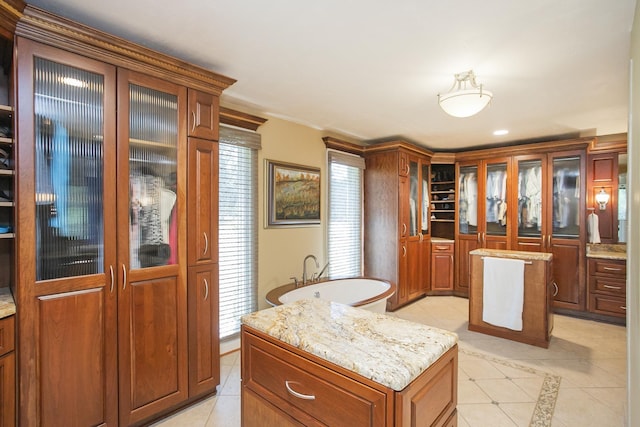 1035 Forest Harbor Dr, Hendersonville, TN 37075 - kitchen featuring light stone counters, light tile patterned floors, glass insert cabinets, a kitchen island, and brown cabinetry
