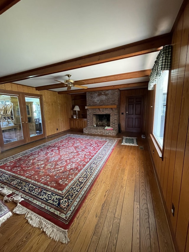living room featuring ceiling fan, a fireplace, wooden walls, beam ceiling, and wood finished floors