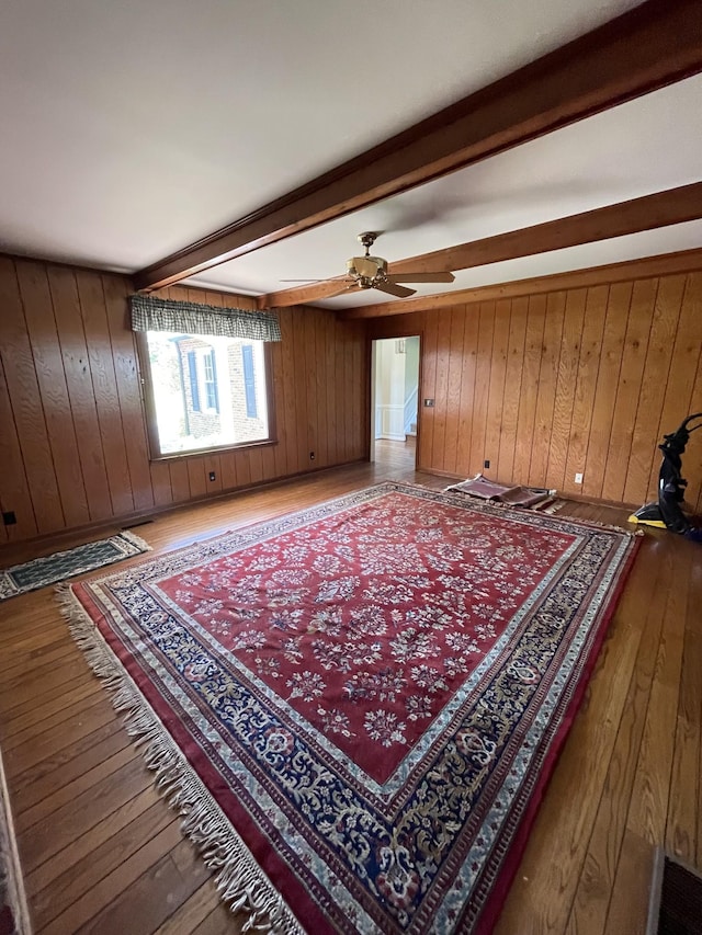 living area featuring wooden walls, hardwood / wood-style flooring, beam ceiling, and ceiling fan