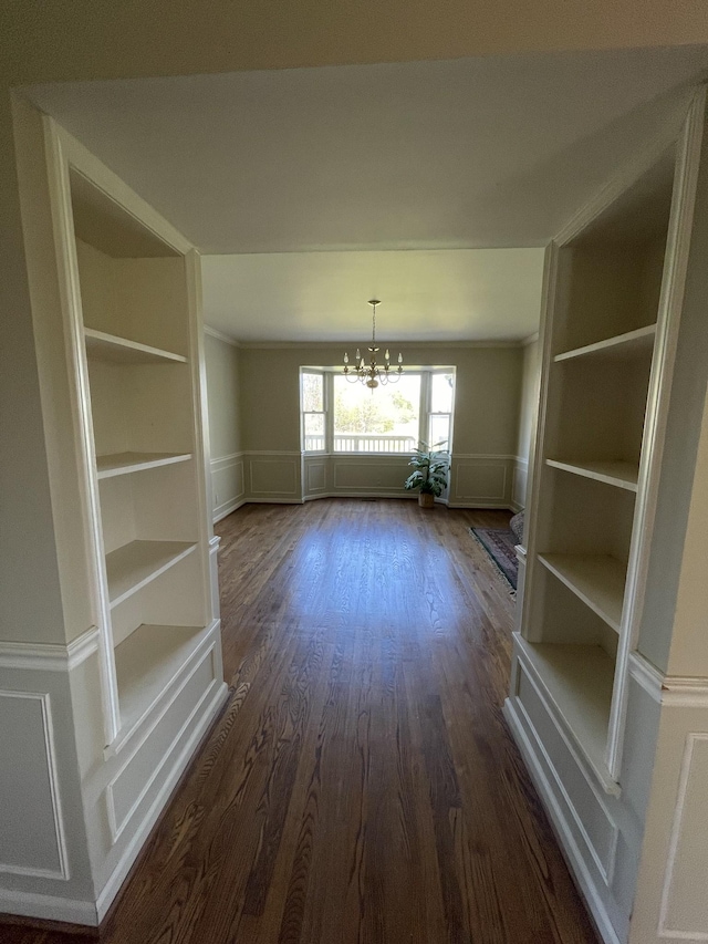 unfurnished dining area featuring a decorative wall, dark wood finished floors, wainscoting, a notable chandelier, and built in shelves