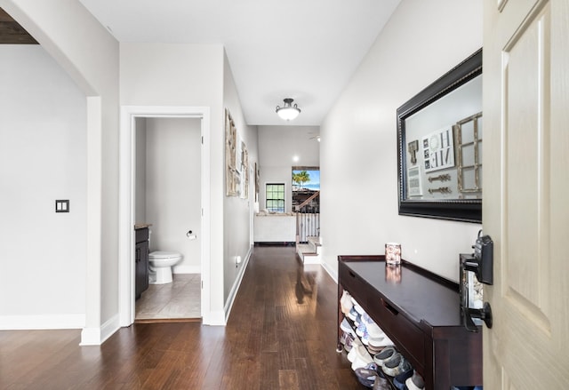 hall with baseboards, wood finished floors, arched walkways, and stairway