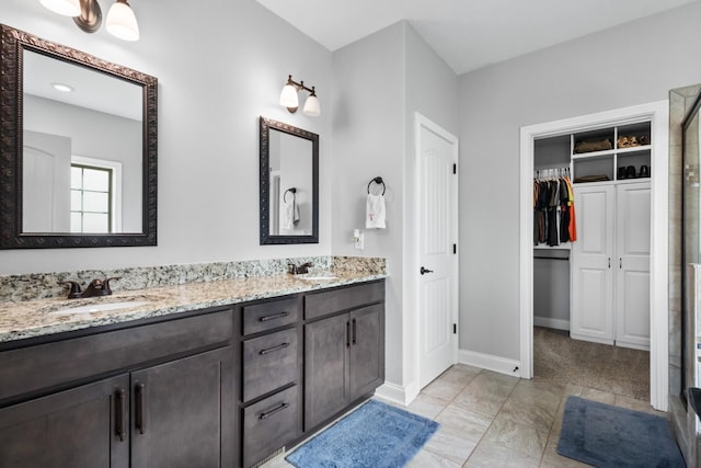 full bath with a walk in closet, baseboards, a sink, and double vanity