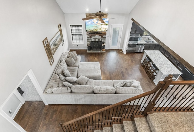 living area with baseboards, a ceiling fan, wood finished floors, stairs, and a wood stove