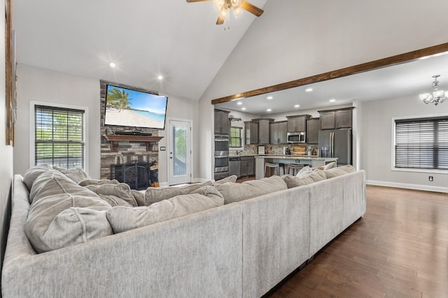 living area featuring a stone fireplace, ceiling fan with notable chandelier, dark wood finished floors, baseboards, and recessed lighting