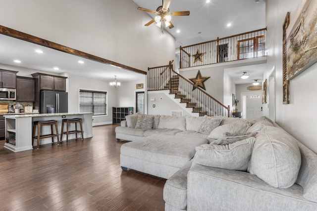 living area featuring recessed lighting, a towering ceiling, stairs, dark wood-style flooring, and ceiling fan with notable chandelier