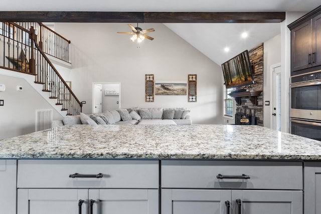 kitchen with open floor plan, beam ceiling, ceiling fan, and stainless steel double oven