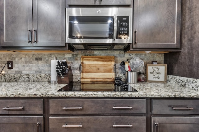 kitchen featuring black electric cooktop, stainless steel microwave, dark brown cabinetry, backsplash, and light stone countertops