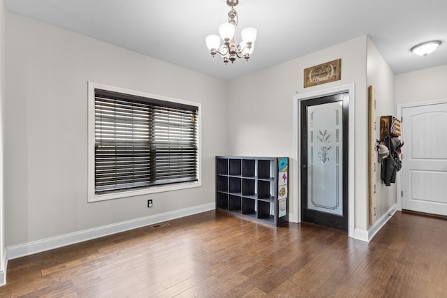 empty room featuring baseboards, wood finished floors, a chandelier, and visible vents