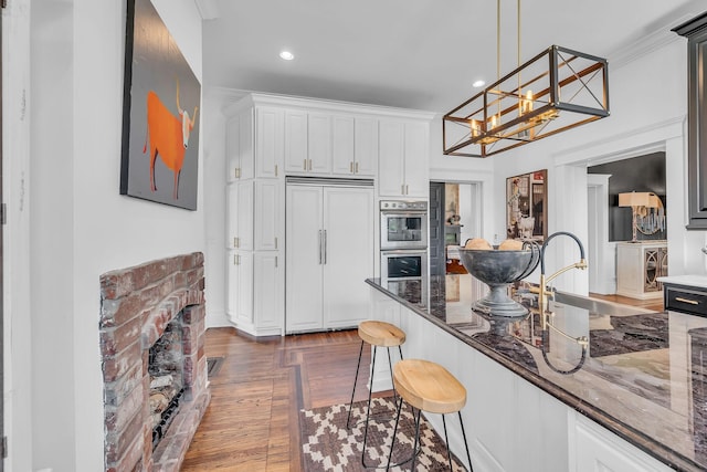 kitchen with a kitchen breakfast bar, stainless steel double oven, dark stone countertops, a sink, and built in refrigerator