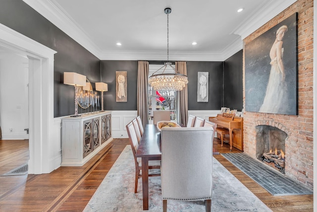 dining room featuring crown molding, a notable chandelier, wood finished floors, and a fireplace