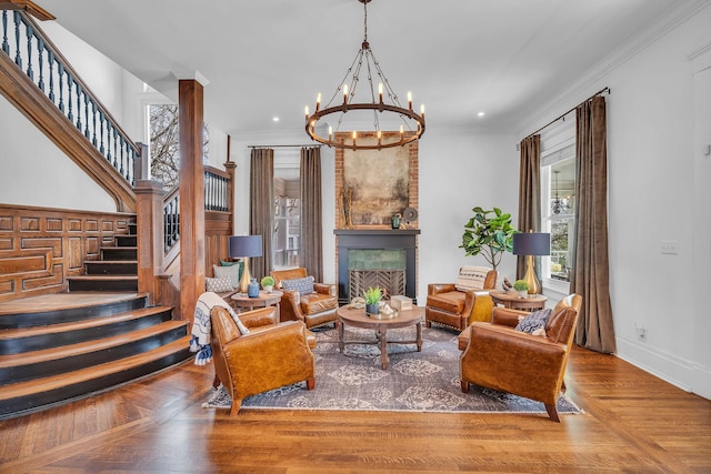 living area with stairway, an inviting chandelier, ornamental molding, baseboards, and a large fireplace