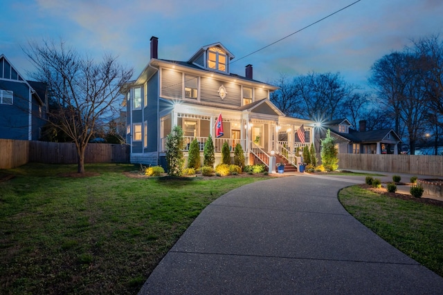view of front facade with a chimney, concrete driveway, fence, a porch, and a front yard