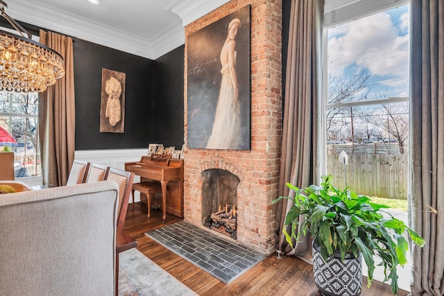 sitting room with wainscoting, a brick fireplace, wood finished floors, and crown molding
