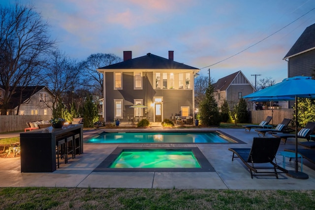 back of house with a chimney, outdoor dry bar, fence, a patio, and an in ground hot tub